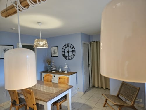Salle à manger de l'appartement Les Ebihens au Clos De La Côte D'émeraude avec table en bois, luminaire suspendu et murs bleus