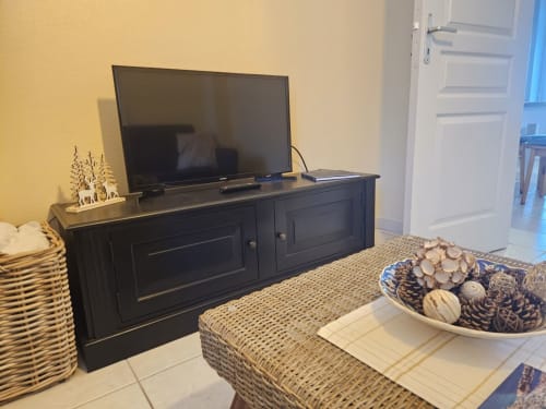 Séjour de l'appartement Les Ebihens à Saint-Benoît-des-Ondes avec meuble TV noir, téléviseur écran plat et mobilier en rotin