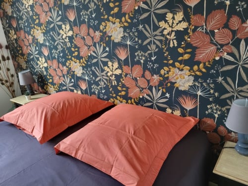 Chambre du gîte au Clos de la Côte d'Émeraude avec coussins corail sur lit foncé et papier peint à motifs floraux