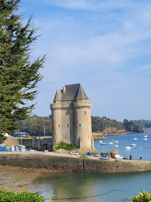 Tour médiévale en pierre au port côtier de Saint-Benoît-des-Ondes, Bretagne, avec bateaux amarrés et arbres persistants