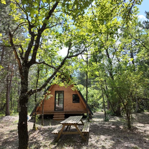 Cabane en A en bois nichée parmi les arbres à l'hôtel spa La Font Vineuse avec table de pique-nique au premier plan