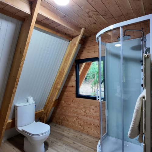 Salle de bain en bois moderne avec douche, toilettes et fenêtre donnant sur le jardin à La Font Vineuse Spa Hotel