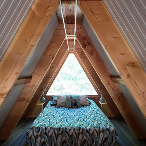 Intérieur de chalet A en bois à La Font Vineuse avec lit, grande fenêtre donnant sur les montagnes et décoration turquoise
