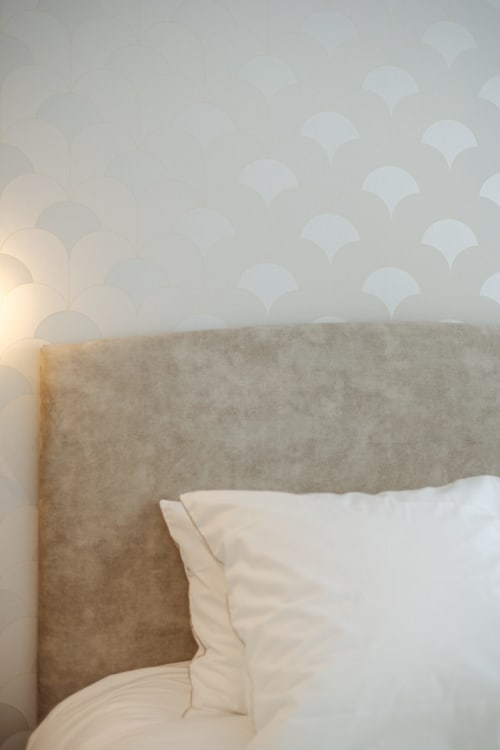 Chambre cosy de L'Ode à Pierre à Dax avec tête de lit capitonnée beige, oreillers blancs et papier peint à motifs.