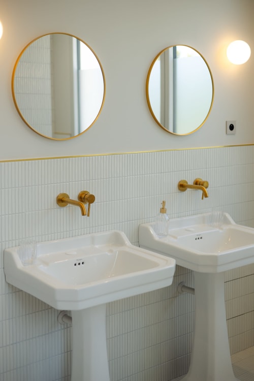 Deux vasques blanches sur piédestal avec robinetterie dorée et miroirs ronds dans la Chambre Coco à L'Ode à Pierre, Dax