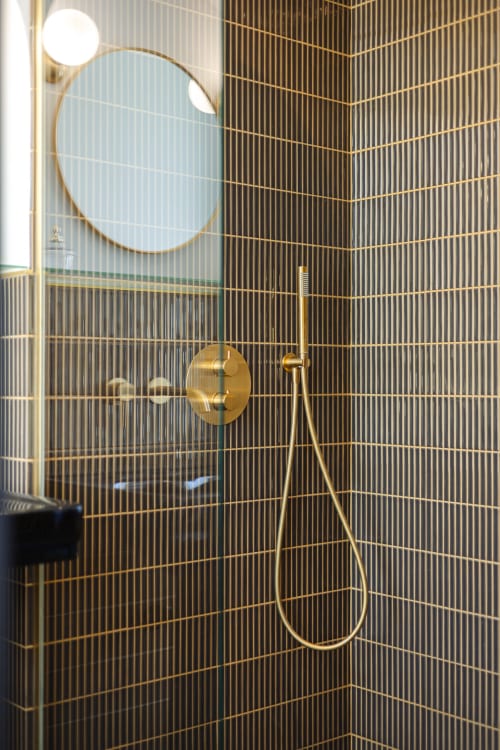 Salle de bains moderne et luxueuse avec carrelage noir cannelé, fixtures en laiton et miroir circulaire à l'hôtel L'Ode à Pierre à Dax