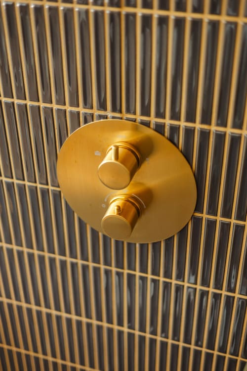 Poignée de mitigeur de douche dorée double montée sur carrelage noir à l'hôtel L'Ode à Pierre à Dax, France