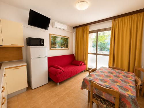 Appartamento con vista mare all'Hotel Anthea, Lignano Sabbiadoro - zona living con divano rosso, cucina e accesso al balcone