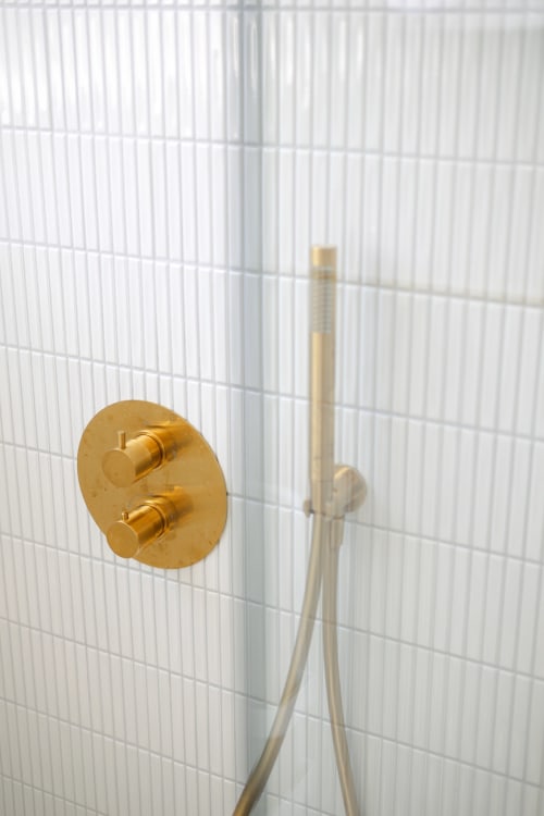 Mitigeur de douche doré double et pomme de douche cascade sur carrelage blanc dans la salle de bain de la Gatsby Room à L'Ode à Pierre, Dax