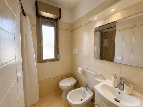 Bagno moderno dell'Anthea Hotel Lignano con doppio lavabo, toilette e rivestimenti in piastrelle decorative