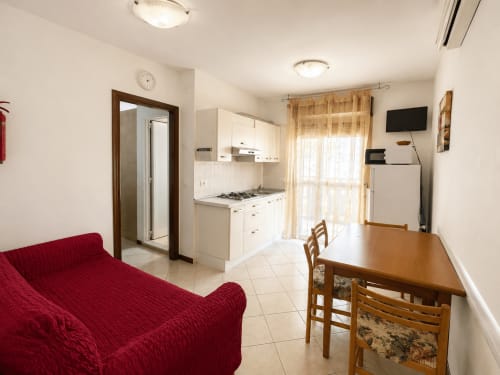 Apartment Timavo 1 dell'Anthea Hotel a Lignano Sabbiadoro con zona living con divano rosso, tavolo da pranzo e cucina a vista