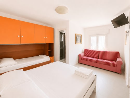 Appartamento Timavo con 2 camere all'hotel Anthea, Lignano Sabbiadoro: letti gemelli, arredamento arancione e divano rosso