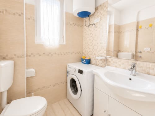 Bagno moderno nell'Appartamento Timavo 2 dell'Hotel Anthea a Lignano Sabbiadoro, con lavandino bianco, lavatrice e piastrelle beige