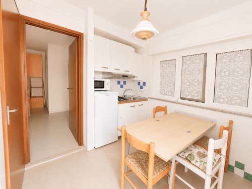 Zona cucina-soggiorno dell'Aparthotel Timavo 2 ad Anthea, Lignano Sabbiadoro, con sedie in legno e mobili bianchi