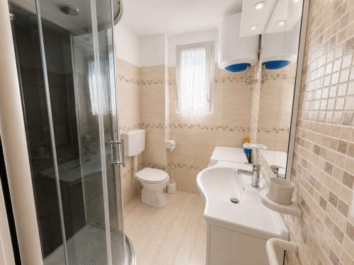 Bagno moderno nell'Appartamento Timavo 2 dell'Hotel Anthea a Lignano Sabbiadoro, con doccia, lavabo e wc con piastrelle beige