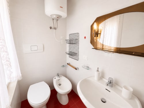Modern bathroom at Anthea hotel in Lignano Sabbiadoro with white fixtures, red tile floor, and gold-framed mirror