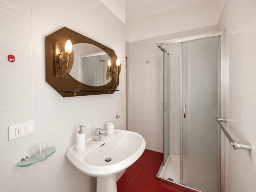 Modern bathroom in Anthea hotel, Lignano Sabbiadoro with pedestal sink, bronze mirror, walk-in shower and red tile flooring