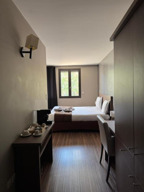 Modern double bedroom at Hôtel de la Bourse in Bagnols-sur-Cèze with city view, dark wood flooring, and contemporary