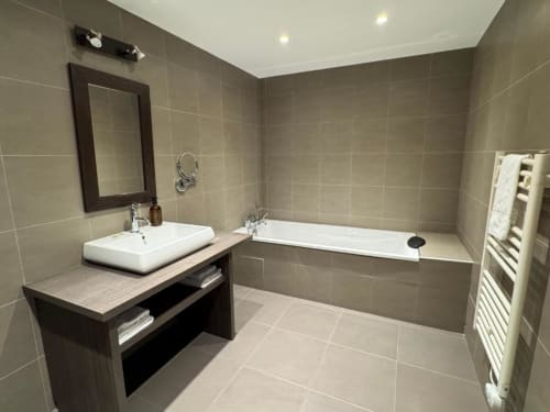 Modern bathroom with beige tile walls, white rectangular sink, and bathtub at Hôtel de la Bourse in Bagnols-sur-Cèze