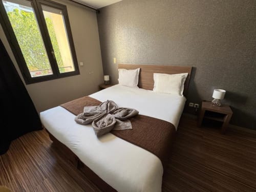 Modern double bedroom at Hôtel de la Bourse in Bagnols-sur-Cèze with white linens, wood furnishings, and city view windows