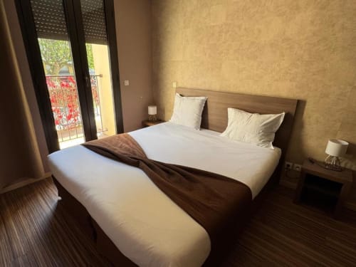 Lit double de la Chambre 3 à l'Hôtel de la Bourse, Bagnols-sur-Cèze, avec balcon vue sur ville et équipements modernes