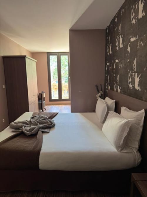Modern double bedroom at Hôtel de la Bourse with city view, brown and beige decor, balcony access, and contemporary
