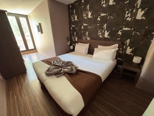 Chambre double moderne à l'Hôtel de la Bourse à Bagnols-sur-Cèze avec literie blanche, mur d'accent à motifs et balcon sur la ville
