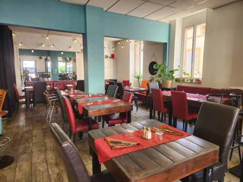 Salle à manger de l'hôtel BDM à Montastruc-la-Conseillère aux murs turquoise, tables en bois, chaises rouges et éclairage décoratif.