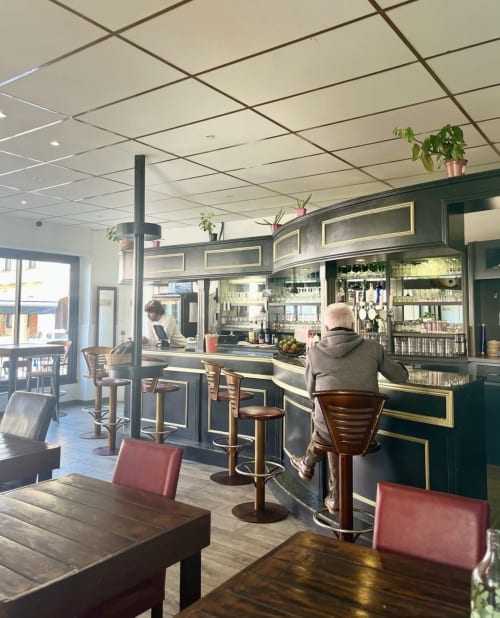 Bar lounge du BDM Hotel à Montastruc-la-Conseillère avec clients assis, mobilier en bois et rangements verts