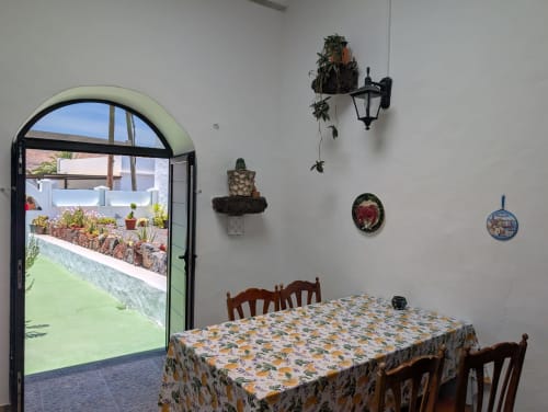 Comedor de la villa Finca Villanueva Lanzarote con vista al jardín a través de puerta arqueada, plantas en maceta y decoraciones de pared