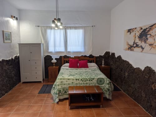 Dormitorio El Recuerdo en Finca Villanueva Lanzarote con cama de madera, almohadas rojas, suelo de baldosas de barro y vistas a las montañas