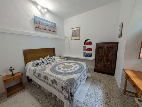 Dormitorio amplio en Finca Villanueva Lanzarote con cama de madera, ropa de cama azul estampada, muebles de madera y paredes blancas