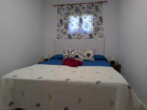 Dormitorio luminoso en Finca Villanueva Lanzarote con cama de acentos azules, cortinas florales y ropa de cama estampada en El Recuerdo