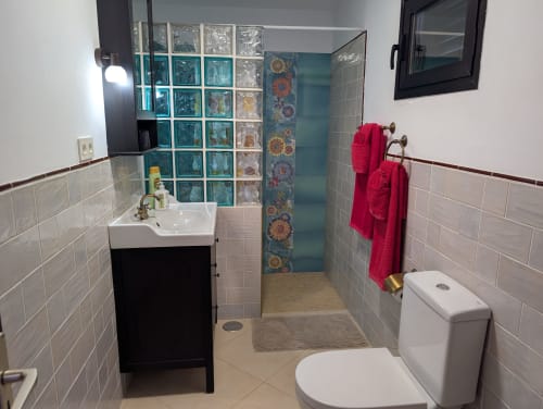 Baño moderno en villa Finca Villanueva Lanzarote con ducha de bloques de cristal, azulejos blancos, toallas rojas y lavabo