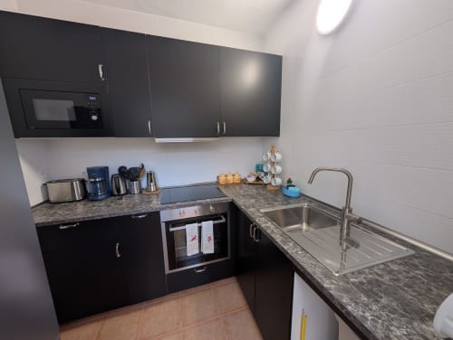 Cocina negra moderna con encimeras de granito, fregadero de acero inoxidable y electrodomésticos en la villa Finca Villanueva Lanzarote