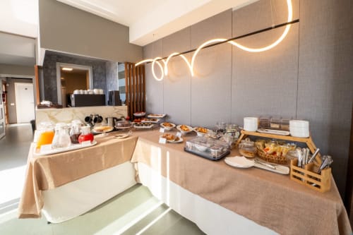 Breakfast buffet setup in Hotel Belvedere Resort's Junior Suite with pastries, juices, and modern neon lighting in