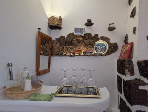 Zona de bar rústica con pared de corcho, piedras decorativas, exhibición de camión de bomberos, copas de vino y decoración local de Lanzarote