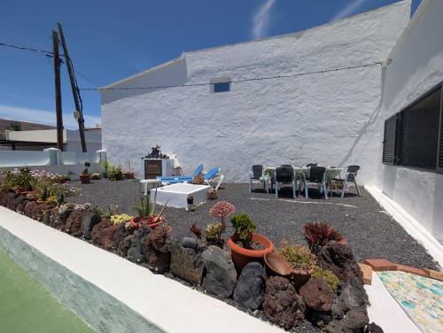 Patio de la villa Finca Villanueva en Mala, Lanzarote con casa de paredes blancas, suculentas, zona de descanso y vistas a las montañas.