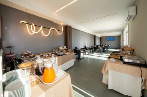 Modern hotel breakfast buffet room at Hotel Belvedere Resort with pastries, juice, tableware and dining tables ready for