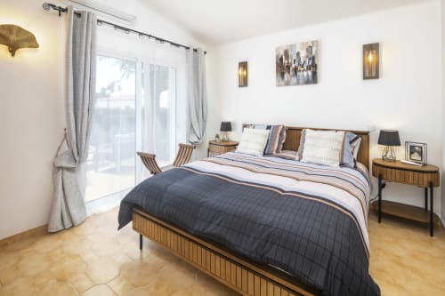 Modern bedroom at MarVillas Rentals in Lagoa with wooden bed, striped bedding, nightstands, and balcony access to natural