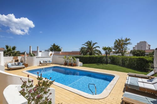 Luxury villa pool in Lagoa with loungers, palm trees, and white-washed architecture under blue sky