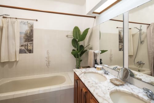 Bright bathroom at MarVillas Rentals in Lagoa with dual sinks, marble countertop, bathtub, and green plant decor