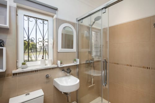 Modern bathroom with beige tiles, walk-in shower, wall-mounted sink, window with decorative grille at MarVillas Rentals,