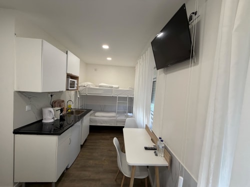 Modern hostel room at Vila Alexandra with kitchenette, bunk beds, wall-mounted TV, and minimalist furnishings in Costa da