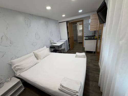 Modern hostel room at Vila Alexandra in Costa da Caparica with queen bed, TV, desk, and kitchenette
