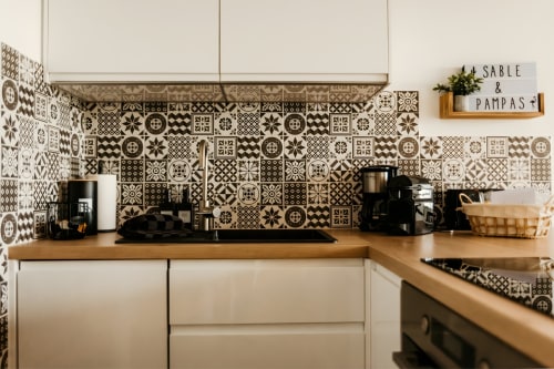 Cuisine moderne avec carrelage noir et blanc géométrique, plan de travail en bois et armoires blanches à l'appartement Sable & Pampas