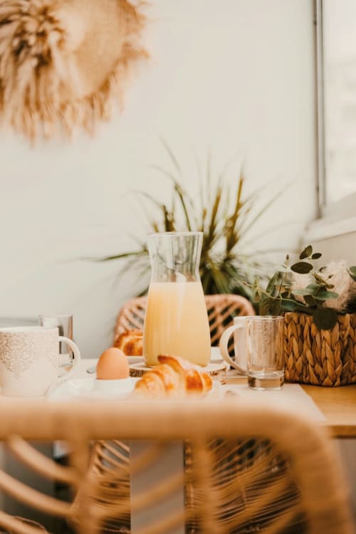 Table de petit-déjeuner au Sable & Pampas avec croissants frais, jus d'orange et plantes en pots à Carnon-Plage