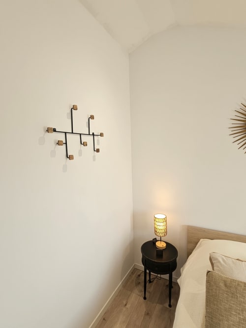 Coin chambre moderne dans une villa corse avec lit en bois, table de nuit noire, lampe tissée et art mural contemporain