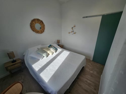 Chambre lumineuse avec lit blanc, vue sur la mer, miroir tressé, table de nuit en bois et porte verte à la villa Altezza à Brando