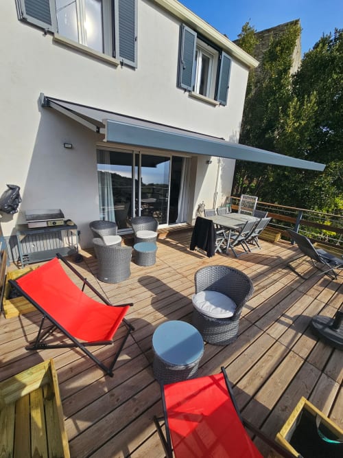 Spacieuse terrasse de villa corse avec vue sur mer, transats rouges, sièges en rotin, table à manger et store rétractable
